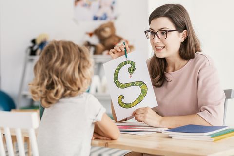 Eine Erzieherin zeigt einem Mädchen den Buchstaben S auf einem Blatt Papier